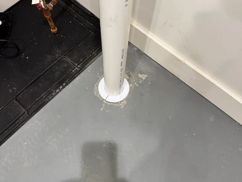 Radon suction pipe rising from a sealed hole in a basement floor