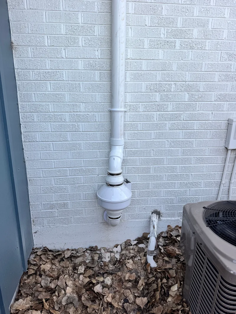 Radon fan mounted low on a painted brick wall beside an AC unit