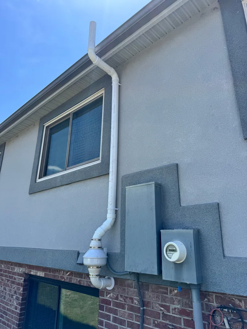 Radon mitigation fan and white vent pipe installed on the side of a two-story Colorado home