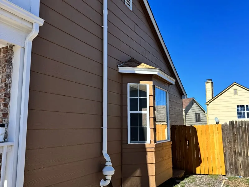 Radon vent pipe running up the corner of a home with brown siding