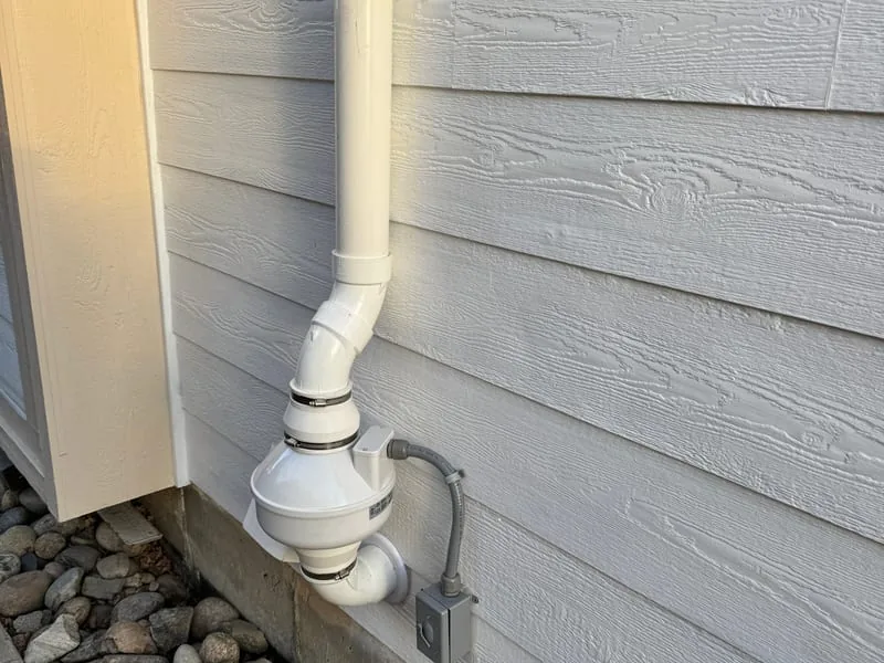 Radon fan mounted on exterior siding with the vent pipe running up the wall